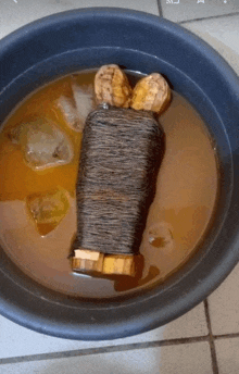 a black bowl filled with brown liquid and ice and a piece of wood wrapped in string
