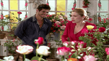 a man and woman are standing in front of a window surrounded by flowers