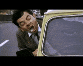 a man in a suit and tie is sticking his head out of a yellow car .