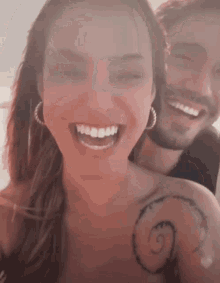 a man and a woman are smiling and the woman has a spiral tattoo on her shoulder
