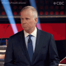 a man in a suit and tie is standing in front of a microphone with the hashtag familyfeud canada