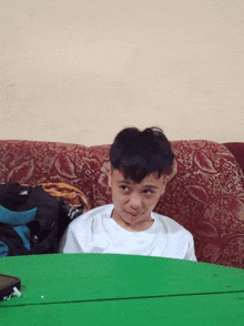 a young boy sitting on a couch with a green table behind him