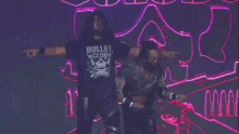 two wrestlers wearing bullet club shirts are walking on a stage