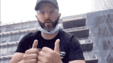 a man wearing a mask and glasses is giving two thumbs up .
