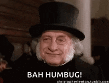 an older man wearing a top hat is smiling and saying bah humbug .