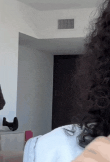 a woman with curly hair is standing in a room with a white wall