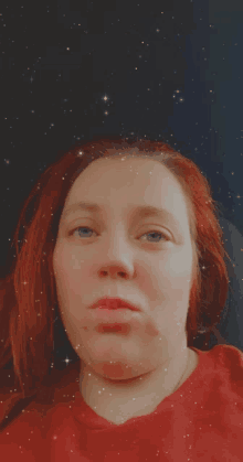 a woman with red hair and blue eyes is wearing a red shirt