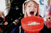 a woman wearing headphones is eating popcorn from an orange bowl