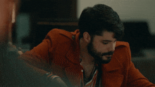a man with a beard is wearing a red coat
