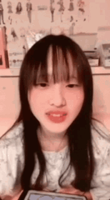 a girl with long hair and bangs is smiling in front of a wall with drawings of women on it