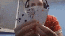 a man wearing headphones and a mask is holding a playing card in front of his face .
