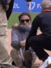 a man is kneeling down on a baseball field and being helped by a man .