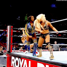 two women are wrestling in a wrestling ring with a royal rumble sign in the background .