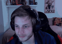 a man wearing headphones looks at the camera in front of a poster that says you