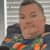 a man wearing a blue shirt with oranges on it is sitting in front of a window