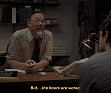 a man sitting at a desk talking to another man with the words but the hours are worse written below him