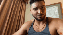 a man with a beard wearing a grey tank top and a gold chain