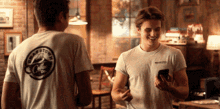 a man wearing a washington coffee co t-shirt smiles while another man looks at his phone