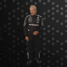 a man in a petronas racing suit stands in front of a black background