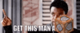 a man is holding a block and pointing at it with the words `` get this man a '' written on it .