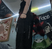 a girl stands in front of a wall with a face tapestry on it