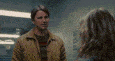 a man in a yellow jacket is standing next to a woman in a room .