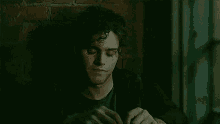 a man with curly hair is sitting in front of a brick wall .
