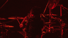 a man playing a guitar in front of a drum set with a red light behind him