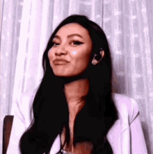 a woman with long black hair is standing in front of a white curtain making a funny face .