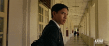 a man in a suit is walking down a hallway with kahar written on the bottom right