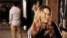 a woman with long blonde hair is standing in a hallway with a man in the background .