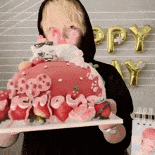 a man in a black hoodie is holding a cake with strawberries on it .