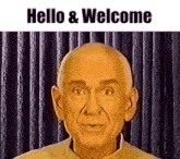 a bald man is standing in front of a curtain and says hello and welcome .