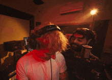 a man wearing headphones stands next to another man in front of a microphone