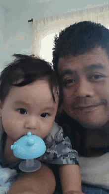 a man is holding a baby with a blue pacifier in his mouth