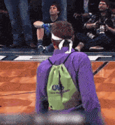 a man wearing a purple shirt and a green backpack with the word owl on it