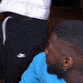 a man with a beard is wearing a blue shirt and earrings while sitting next to another man .