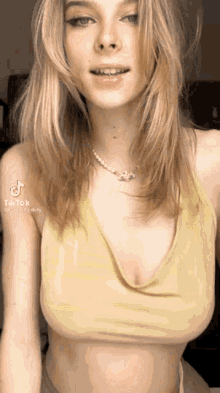 a woman wearing a yellow crop top and a pearl necklace is looking at the camera .