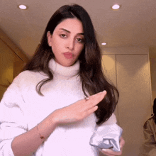 a woman wearing a white sweater is holding a bag