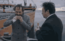 two men are eating food in front of a boat