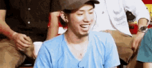 a man wearing a baseball cap and a blue shirt is laughing while sitting in a stadium .