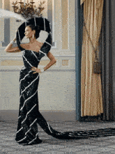 a woman in a long black and white dress stands in front of a window
