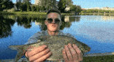 a man wearing sunglasses is holding a large fish in his hands
