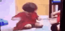 a little girl in a red dress is sitting on the floor in front of a tv .