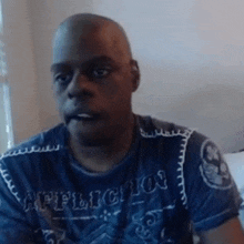 a bald man wearing a blue shirt that says affliction