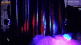 a man in a mask is walking through a dark room with purple lights behind him .