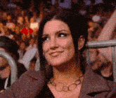 a woman wearing a necklace is smiling in front of a crowd of people