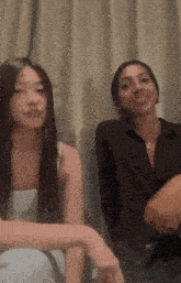 two women are sitting next to each other in front of a window .