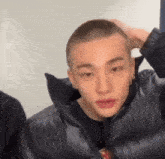 a young man with a shaved head is wearing a black jacket and holding his head .