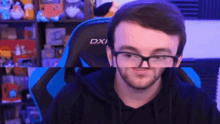 a man wearing glasses is sitting in a blue gaming chair